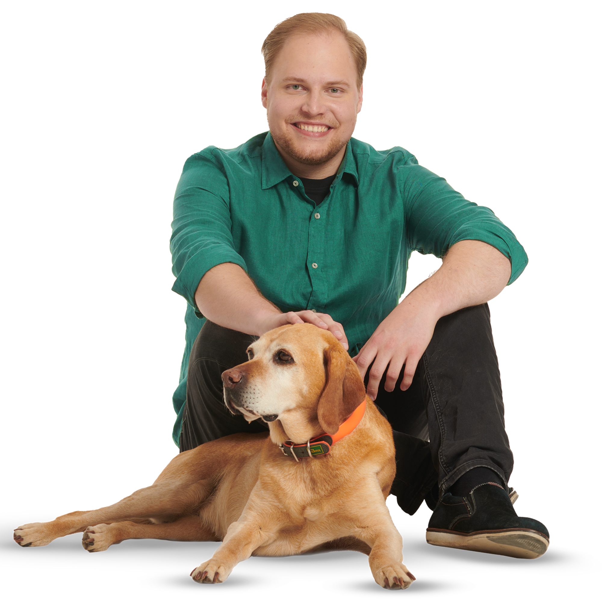 Ein junger Mann in dunkelgrünem Hemd und mit Hund sitzt auf dem Boden.