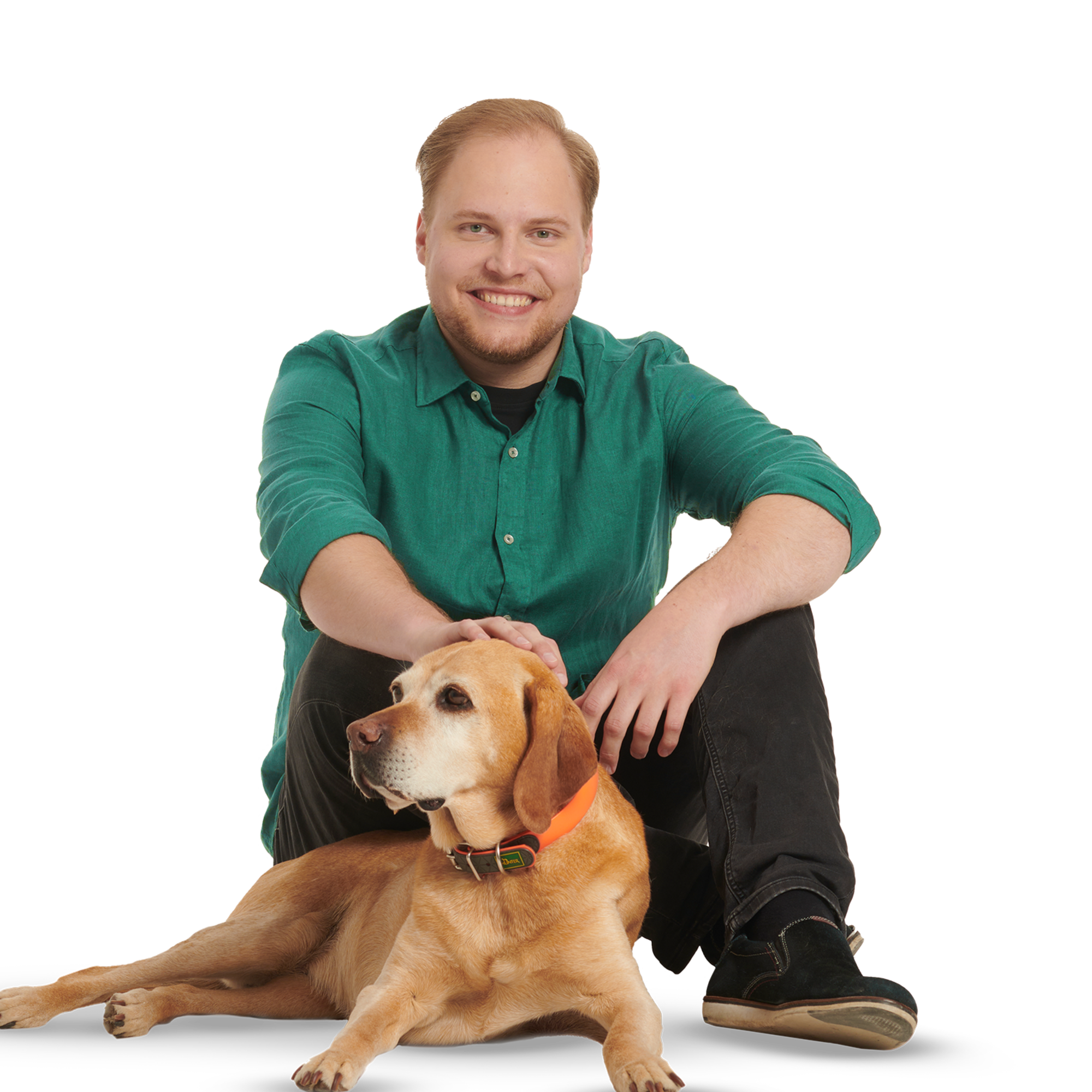 Ein junger Mann in dunkelgrünem Hemd und mit Hund sitzt auf dem Boden.