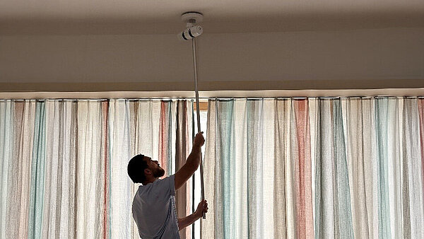 Ein Mann in Pfegekleidung hält einen Stab mit einem technischen Gerät nach oben, Richtung Decke.