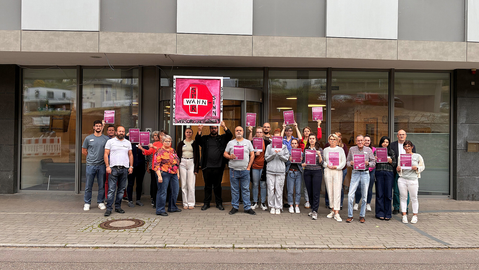 Eine Gruppe von Menschen, die Plakate hochhalten, stehen vor einem Gebäude.