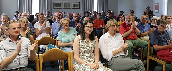 Rund 70 Menschen sitzen in einem Vortragsraum und klatschen.