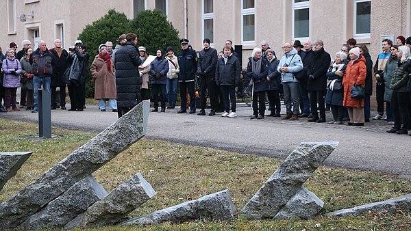 Im Vordergrund ist das Mahnmal aus schräg stehenden Granitstelen zu sehen, im Hintergrund die Teilnehmenden des Gedenktags am 27. Januar 2026.