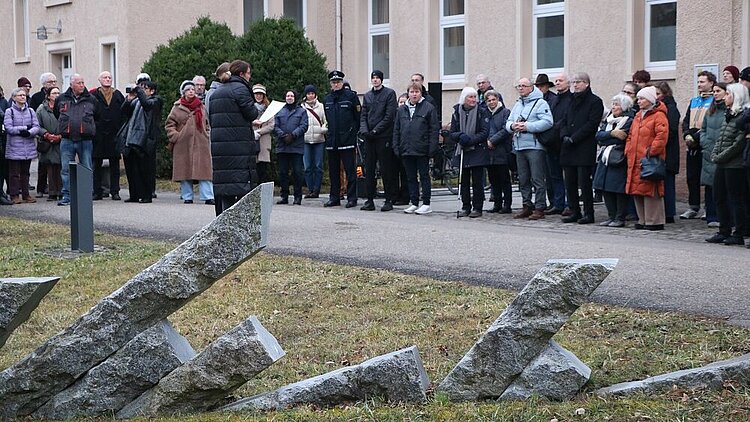 Im Vordergrund ist das Mahnmal aus schräg stehenden Granitstelen zu sehen, im Hintergrund die Teilnehmenden des Gedenktags am 27. Januar 2026.