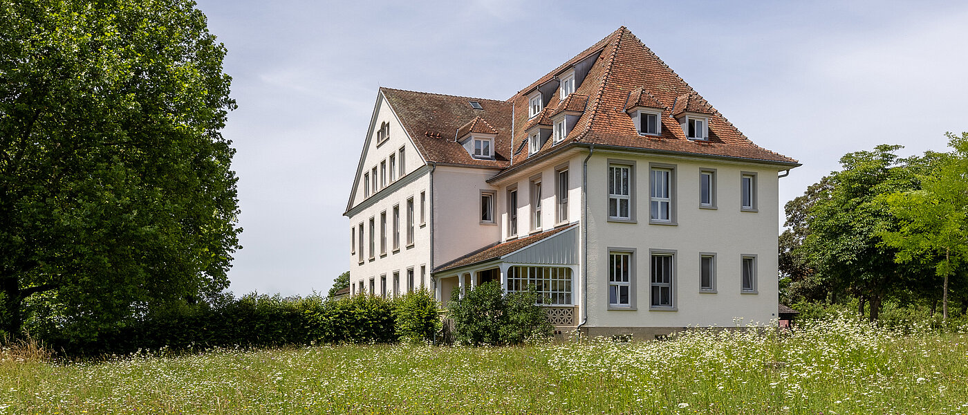 Historisches Gebäude mit Wintergarten und blühender grüner Wiese davor.