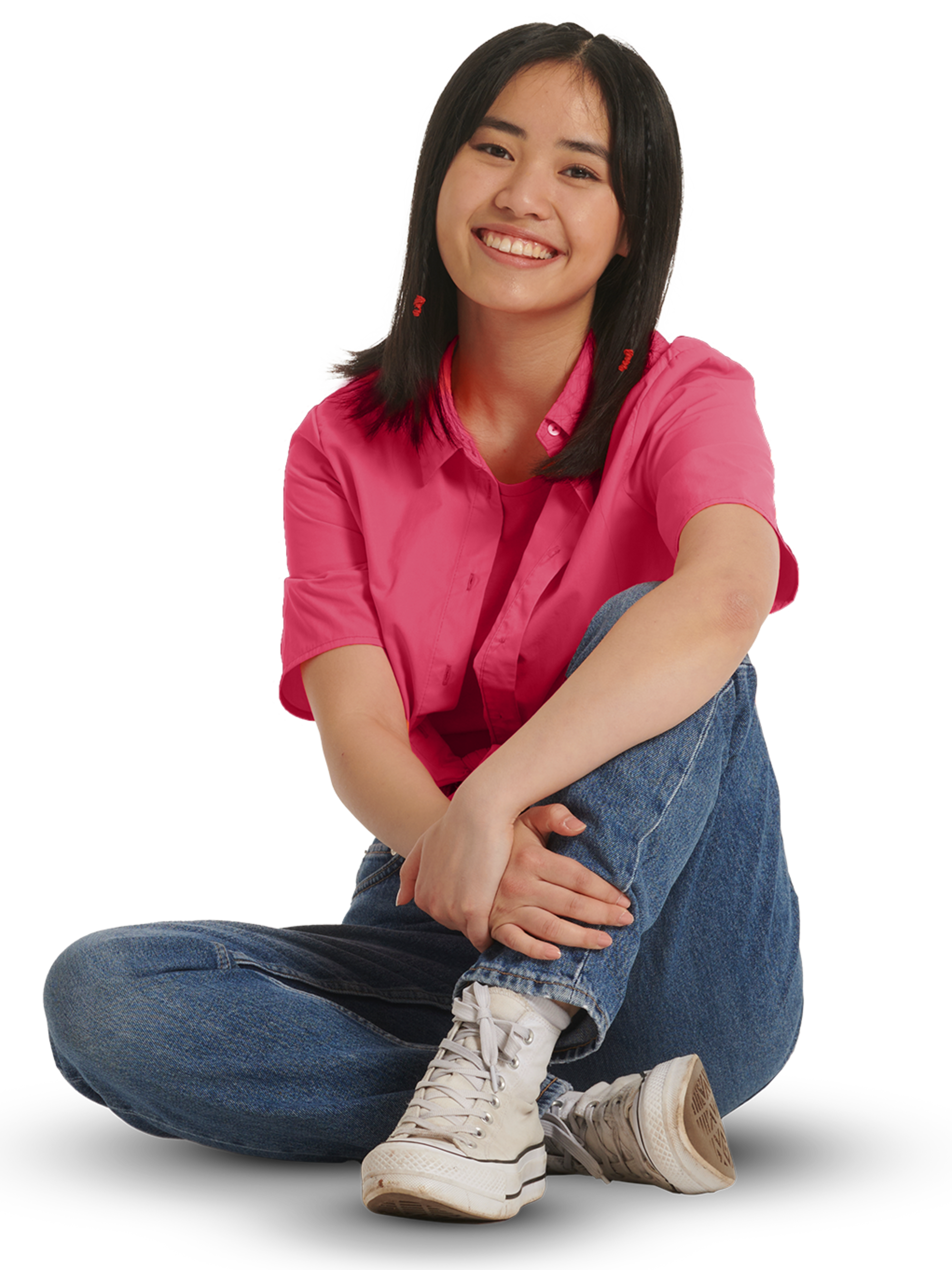 Ein junges Mädchen in pinker Bluse und Jeans sitzt auf dem Boden.