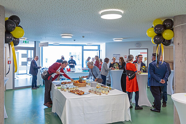 Menschen in einem mit Ballons geschmückten Raum und Tischen mit Essen.
