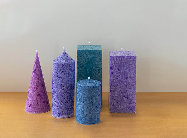 Lilane, blaue und grüne Kerzen in unterschiedlichen runden und eckigen Formen.