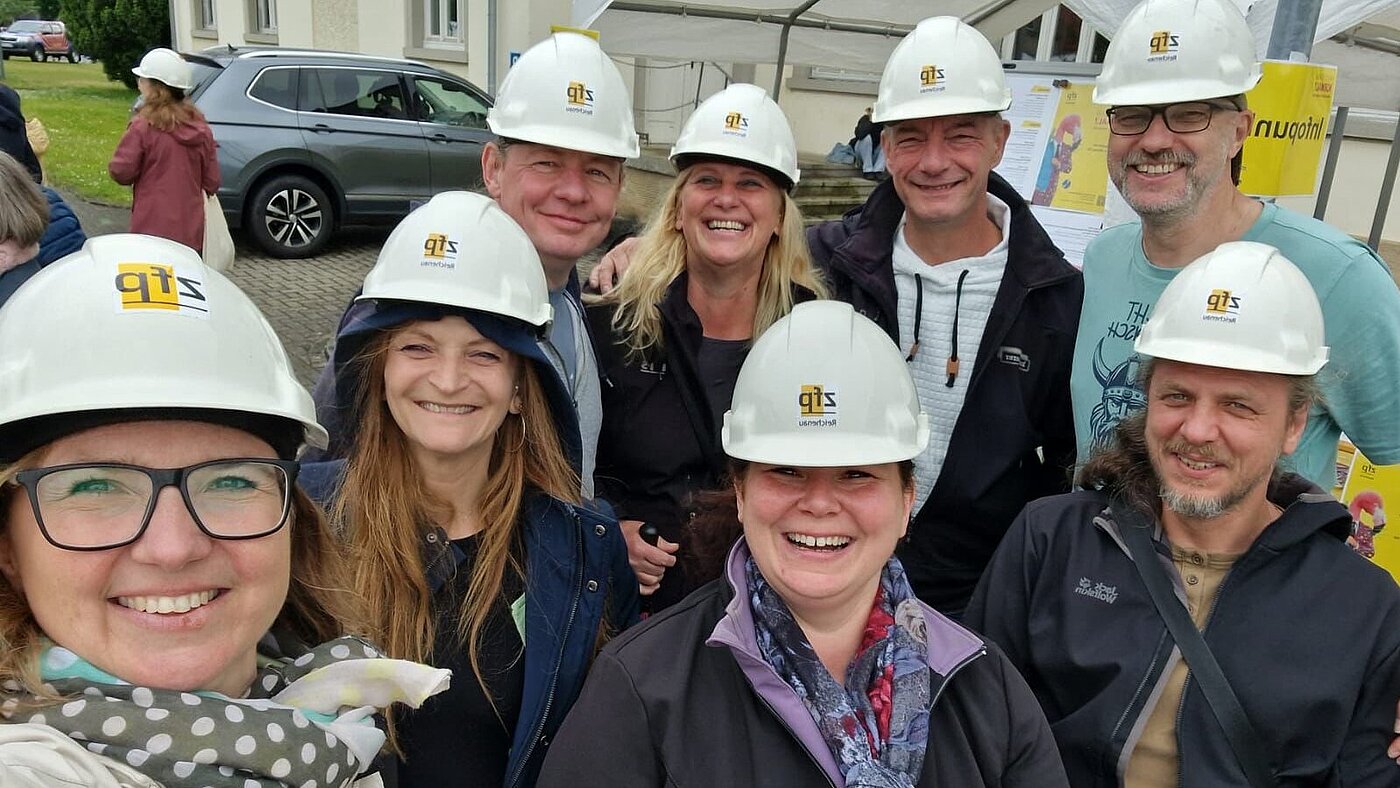 Acht lachende Menschen, die Bauhelme tragen, freuen sich eine Führung durch die Versorgungstunnel des ZfP Reichenau.