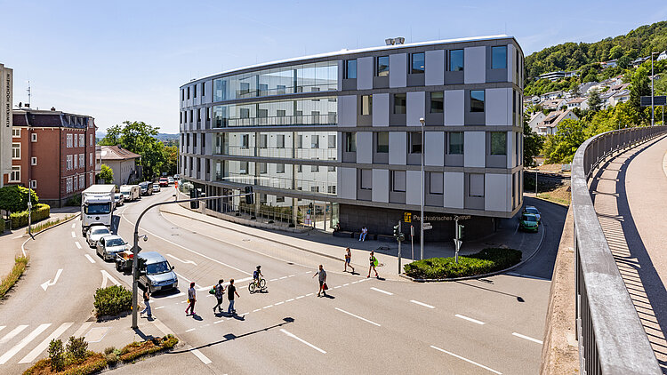 Vierstöckiges, ovales Gebäude aus Glas und Beton im Herzen einer Stadt und an einer Kreuzung gelegen.