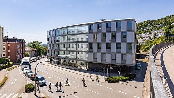Vierstöckiges, ovales Gebäude aus Glas und Beton im Herzen einer Stadt und an einer Kreuzung gelegen.