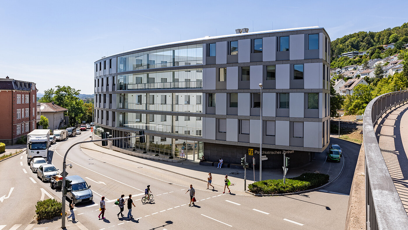 Vierstöckiges, ovales Gebäude aus Glas und Beton im Herzen einer Stadt und an einer Kreuzung gelegen.