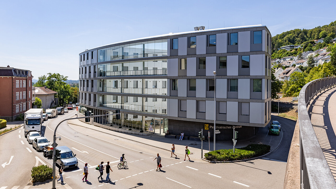 Vierstöckiges, ovales Gebäude aus Glas und Beton im Herzen einer Stadt und an einer Kreuzung gelegen.