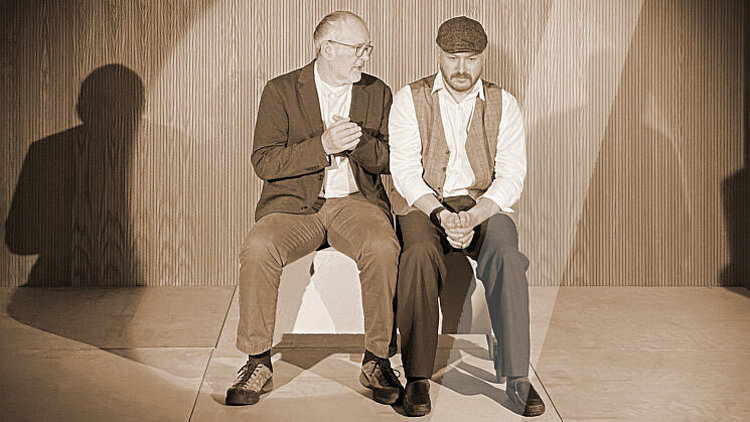 Zwei Männer sitzen nebeneinader und sind ins Gespräch vertieft.