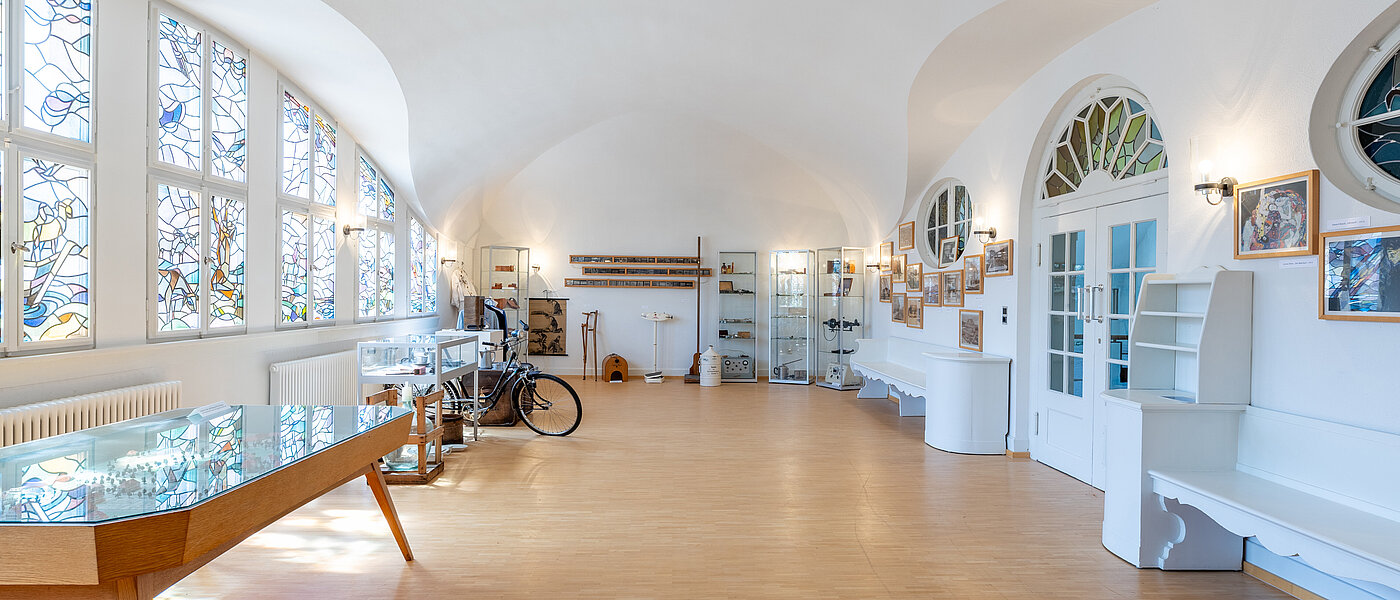 Museumsraum mit einem großen Kirchenfenster und verschiedenen Ausstellungsstücken.