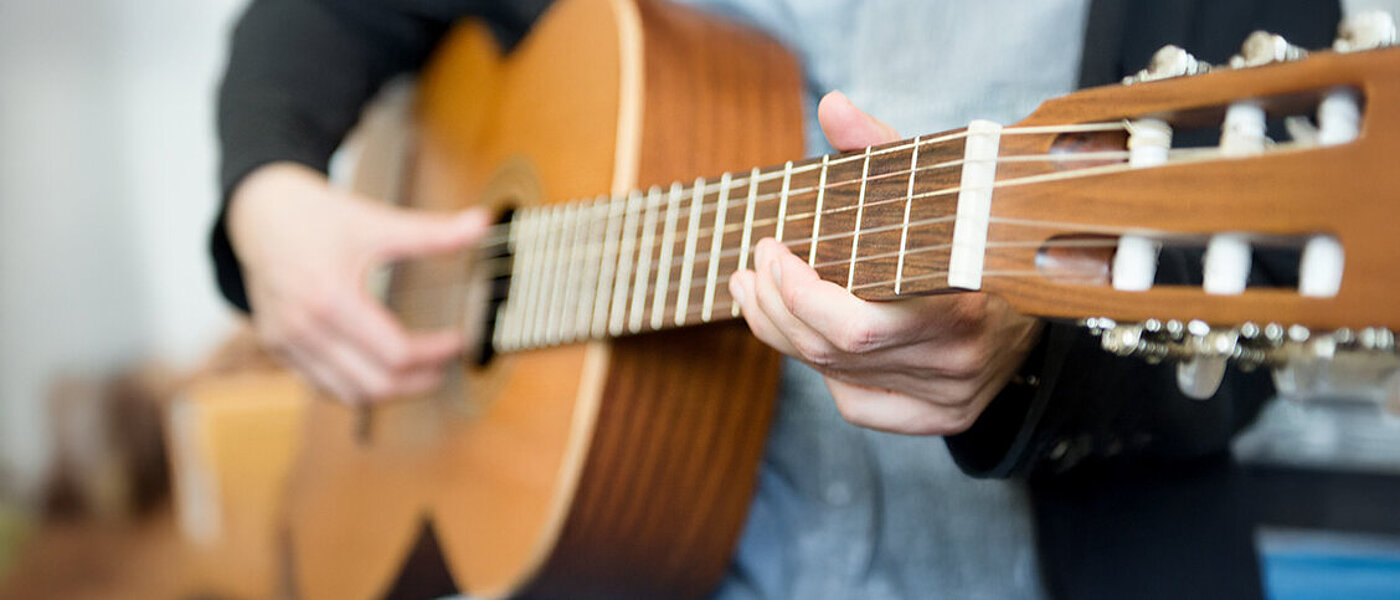 Detailaufnahme von einer Frau, die eine Holzgitarre spielt.