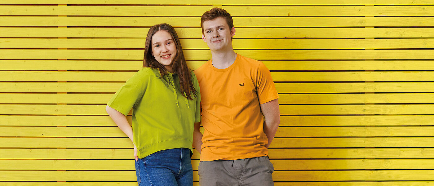 Mädchen und Junge stehen gemeinsam vor einer gelben Wand.