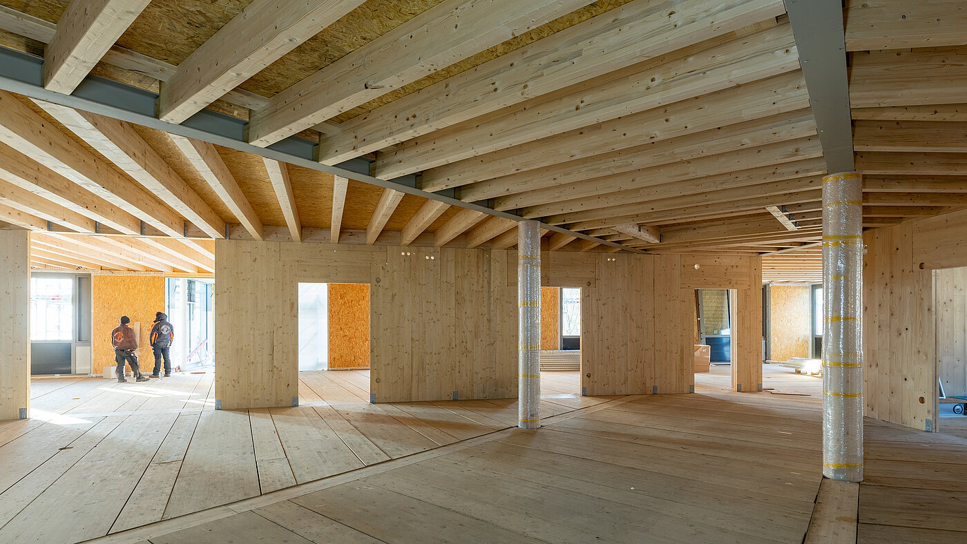 Holzkonstruktion auf einer Baustelle mit zwei Handwerkern im Hintergrund.