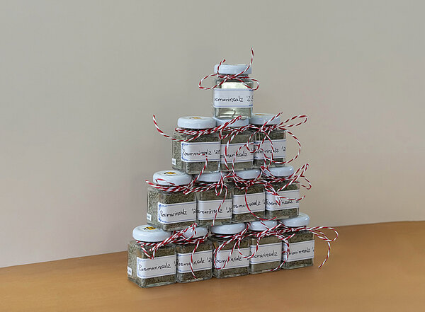 Kleine Gläser mit selbstgemachtem Rosmarinsalz, die eine rote Schleife haben und zu einer Pyramide aufgestapelt sind.