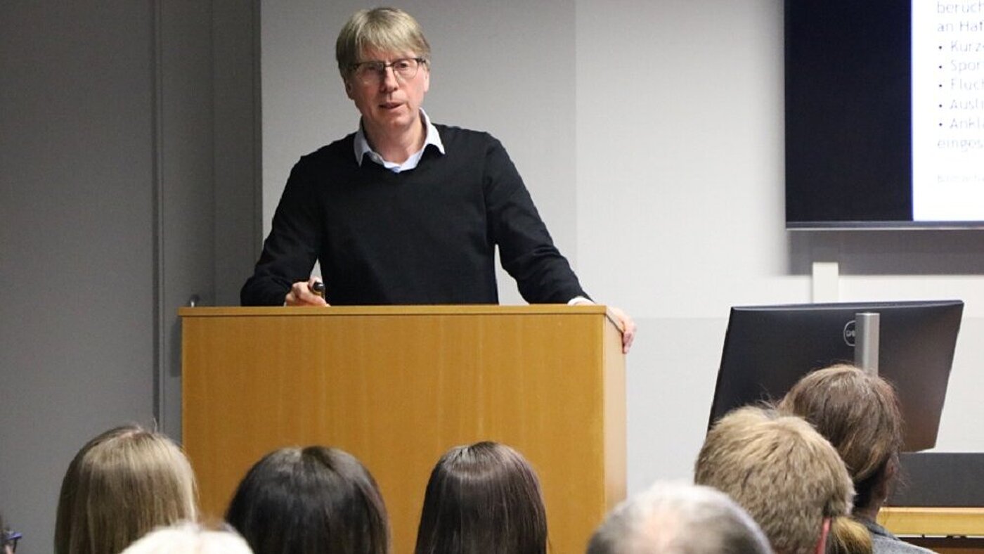 Ein Mann steht an einem Rednerpult und hält einen Vortrag.