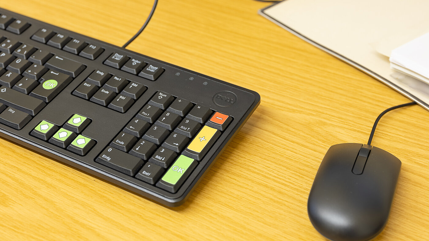 Eine Tastatur mit grünen, gelben und roten Markierungen sowie eine schwarze Computermaus liegen auf einem Tisch.