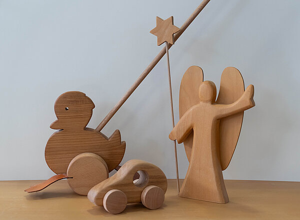 Eine Ente aus Holz, ein hölzernes Auto sowie ein Engel mit Stern in der Hand stehen vor einem weißen Hintergrund.